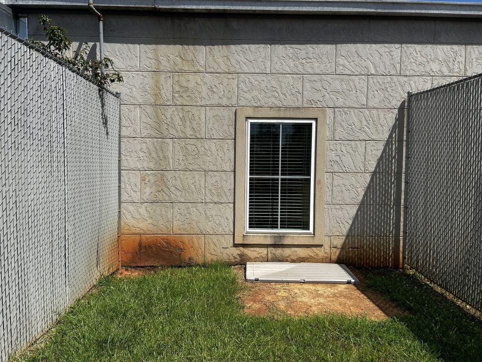Painted block wall with orange rust streaks and grime under a window in a Nashville yard