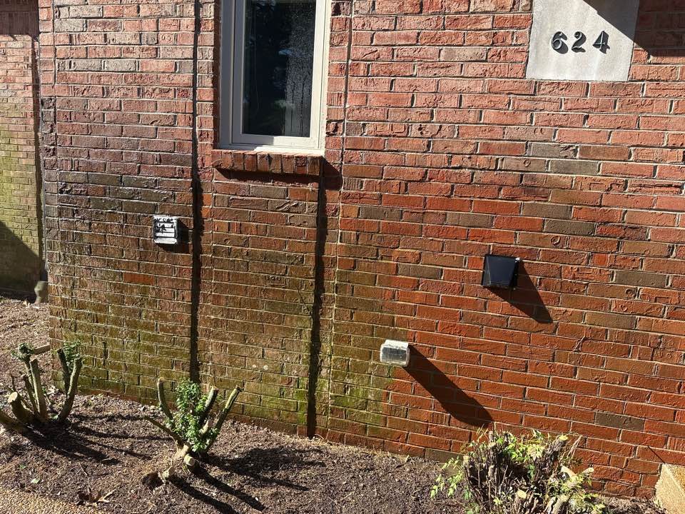 Red brick wall with dark mildew and dirt staining near the ground on a Nashville building